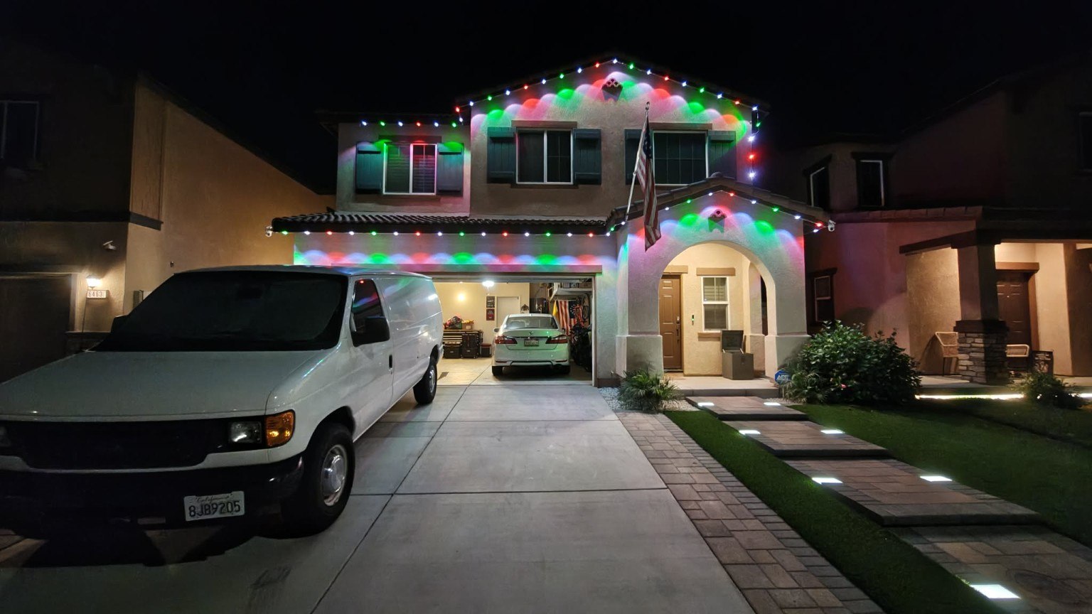 Completed permanent holiday lighting along the roofline of a two-story home, illuminated in red, green, and white