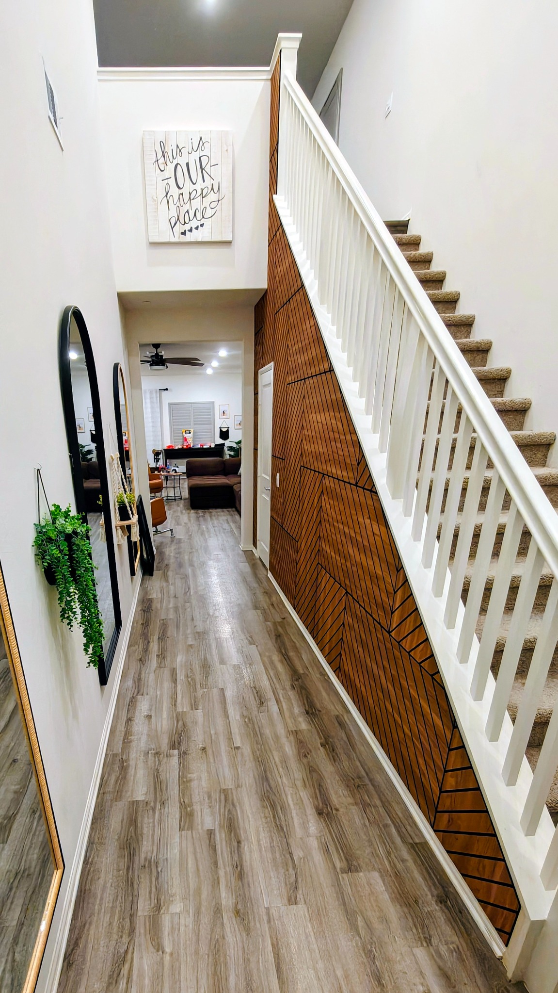 Custom geometric wood accent wall beneath a staircase with installed mirrors and planters