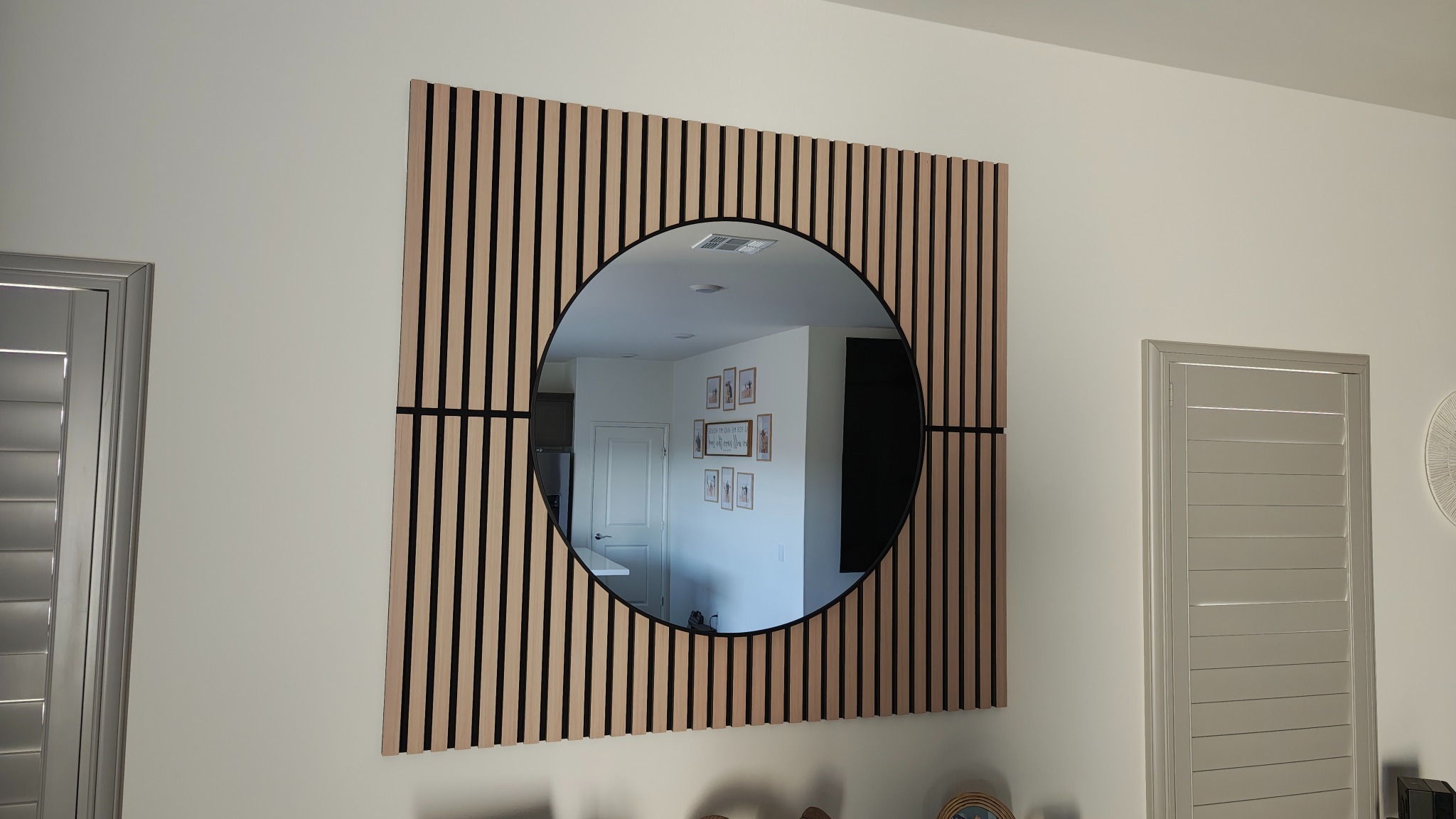Completed wood-slat feature wall with an oversized round mirror